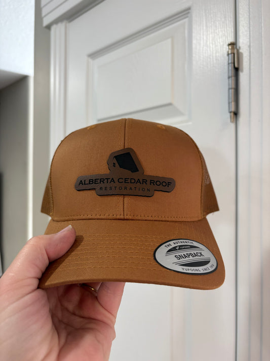 Brown cap held by a hand with visible branding on a white door background